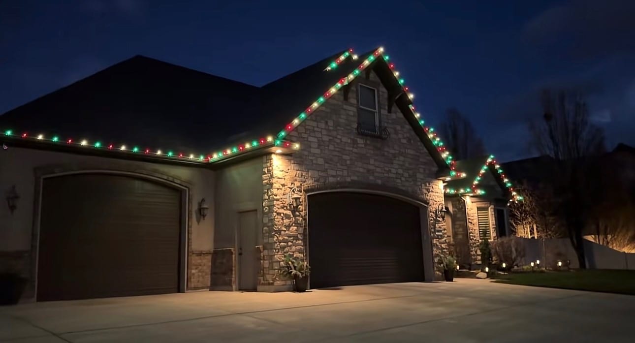 Red, green, and white holiday lights following a home’s roofline and gables at dusk